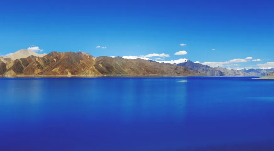 A colorful gallery image of the holy Tsomgo Lake (Changu Lake) with a decorated yak and prayer flags fluttering against the Himalayan backdrop.